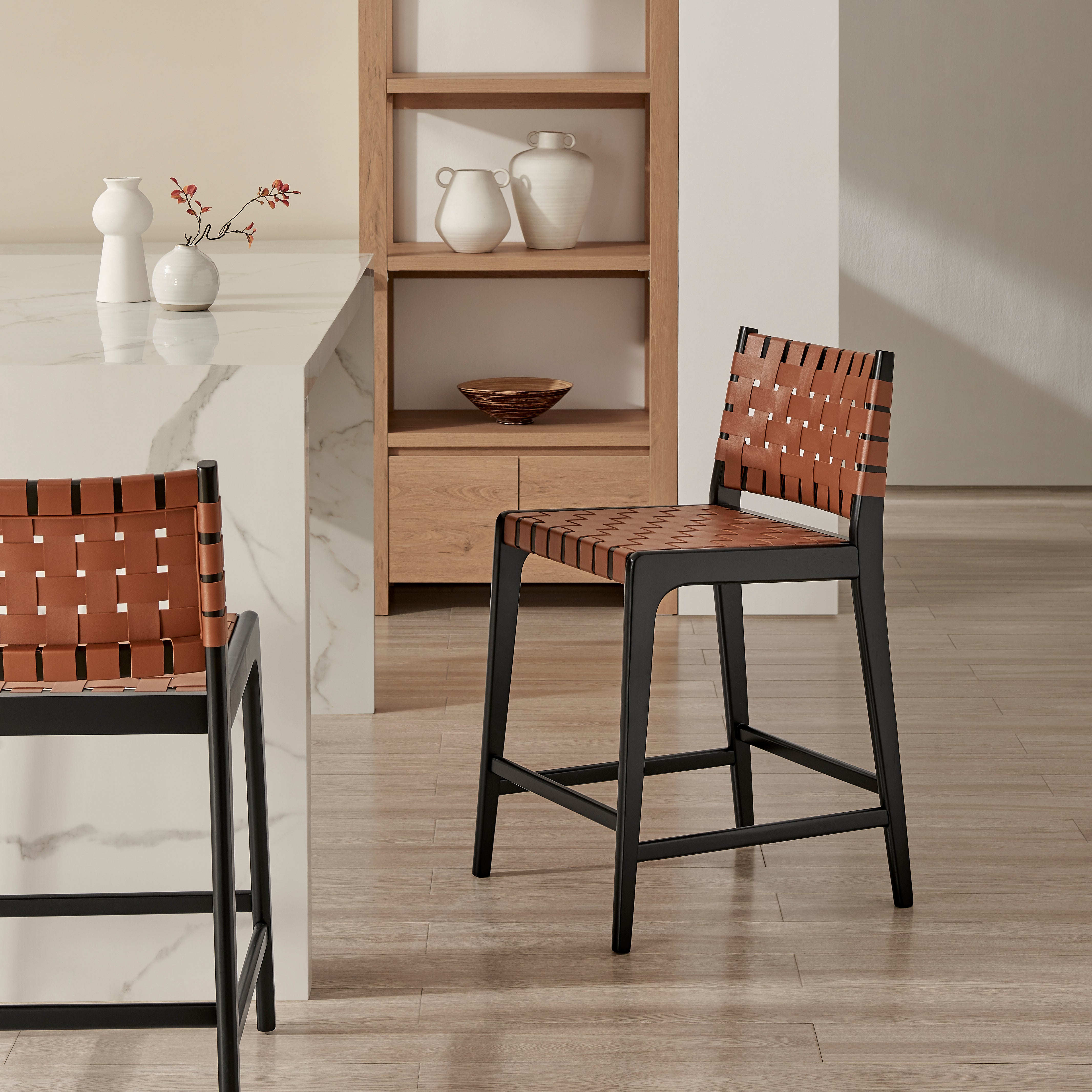 Modern woven faux-leather barstools with black frames styled beside a marble kitchen island in a warm minimalist kitchen.